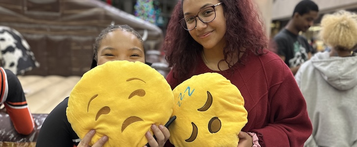 Two students holding emoji pillows